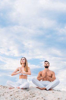 lotus poz (padmasana) ile namaste mudra kabuklarıyla kumlu otururken meditasyon güzel genç çift