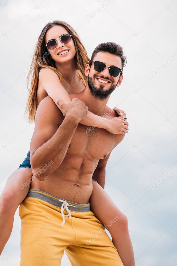 happy young woman piggybacking on boyfriends back in front of cloudy sky