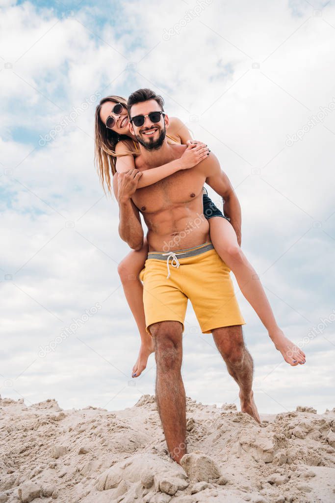 attractive young woman piggybacking on boyfriends back at beach