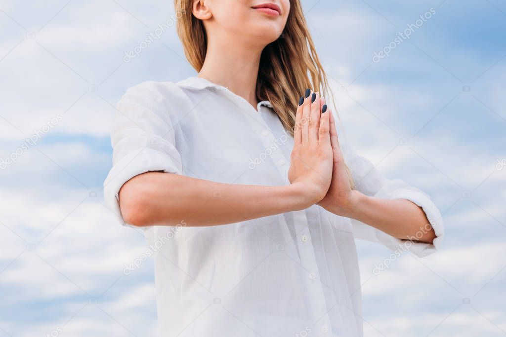 cropped shot of young woman meditating with hands making namaste mudra in front of cloudy sky