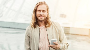 mutlu genç adam earphones ve smartphone Caddesi ve kameraya bakarak ile müzik dinleme