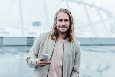 kulaklık ve smartphone Caddesi ve kameraya bakarak ile müzik dinleme yakışıklı genç adam