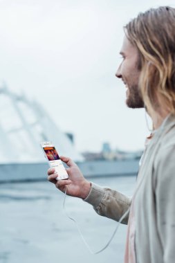 mutlu genç adam sokakta ekranda soundcloud app ile Smartphone kullanarak