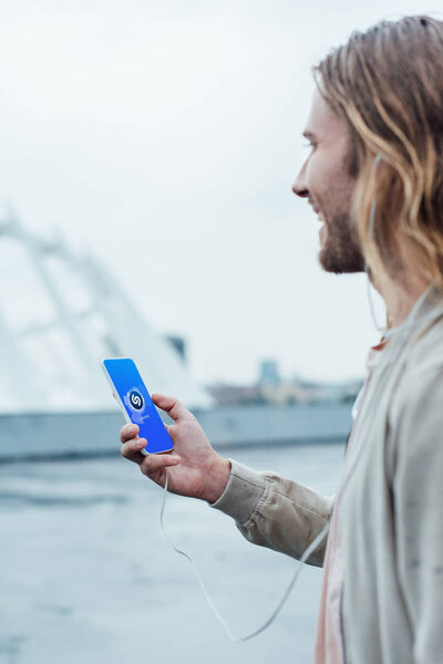 happy young man using smartphone with shazam app on screen on street