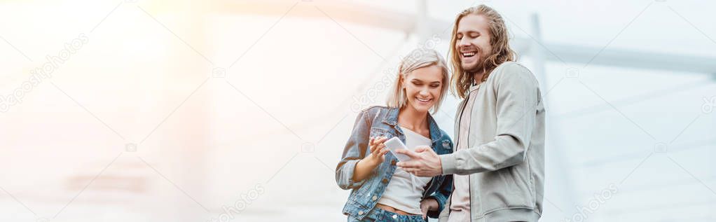 panoramic shot of happy young couple using smartphone together on street