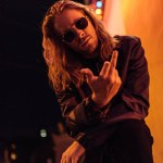 Handsome young man in leather jacket and sunglasses showing middle finger at camera on street at night under yellow light