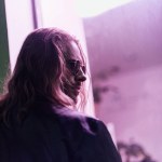 Rear view of handsome young man in leather jacket and sunglasses looking away on street at night under pink light