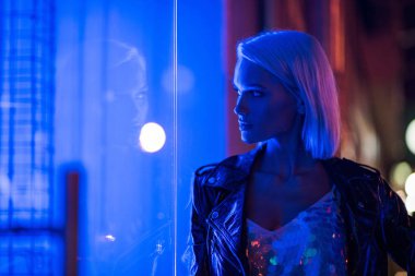 parlak kolsuz bluz ve deri ceket mavi ışık altında geceleri sokakta şık genç kadın