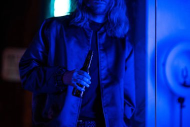 Genç adam kırpılmış atış ile şişe bira gece sokakta mavi ışık altında