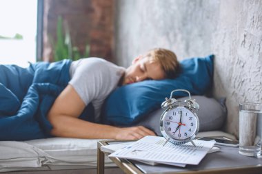 selective focus of alarm clock and sleeping man in bed behind  clipart