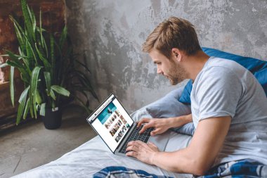 Genç adam yatakta dizüstü ekran üzerinde amazon Web ile kullanma