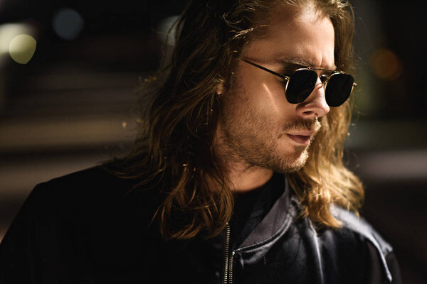 close-up portrait of handsome young man in sunglasses and leather jacket on street at night