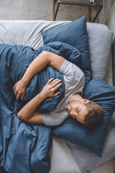 overhead view of young handsome man sleeping under blanket in his bed at home