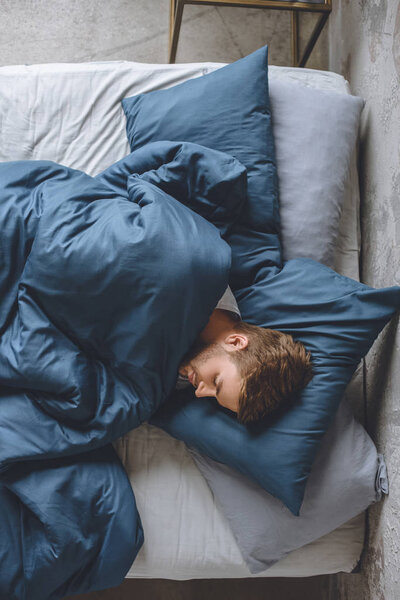 top view of young handsome man sleeping under blanket in his bed at home
