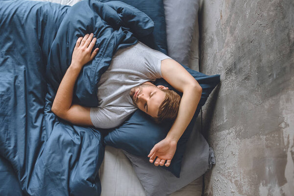 elevated view of young handsome man sleeping under blanket in his bed at home