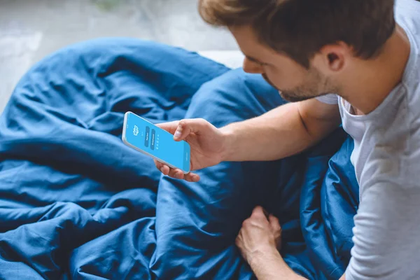 画面の Skype ではスマート フォンを使用してベッドで若い男の選択と集中 — ストック写真