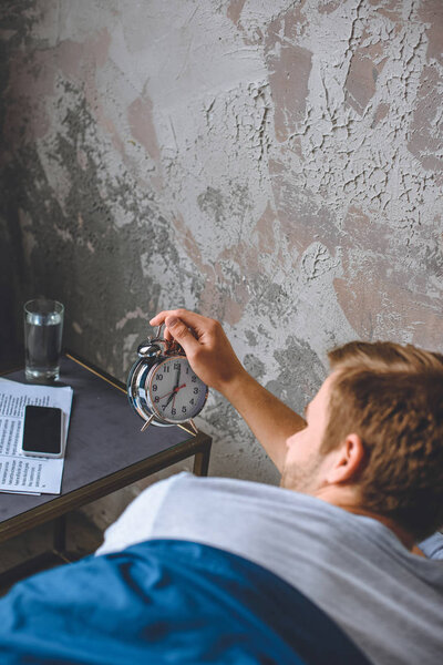 young man in bed turning off alarm clock at home