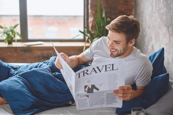 Smiling Young Man Reading Travel Newspaper Bed Home — Stock Photo, Image