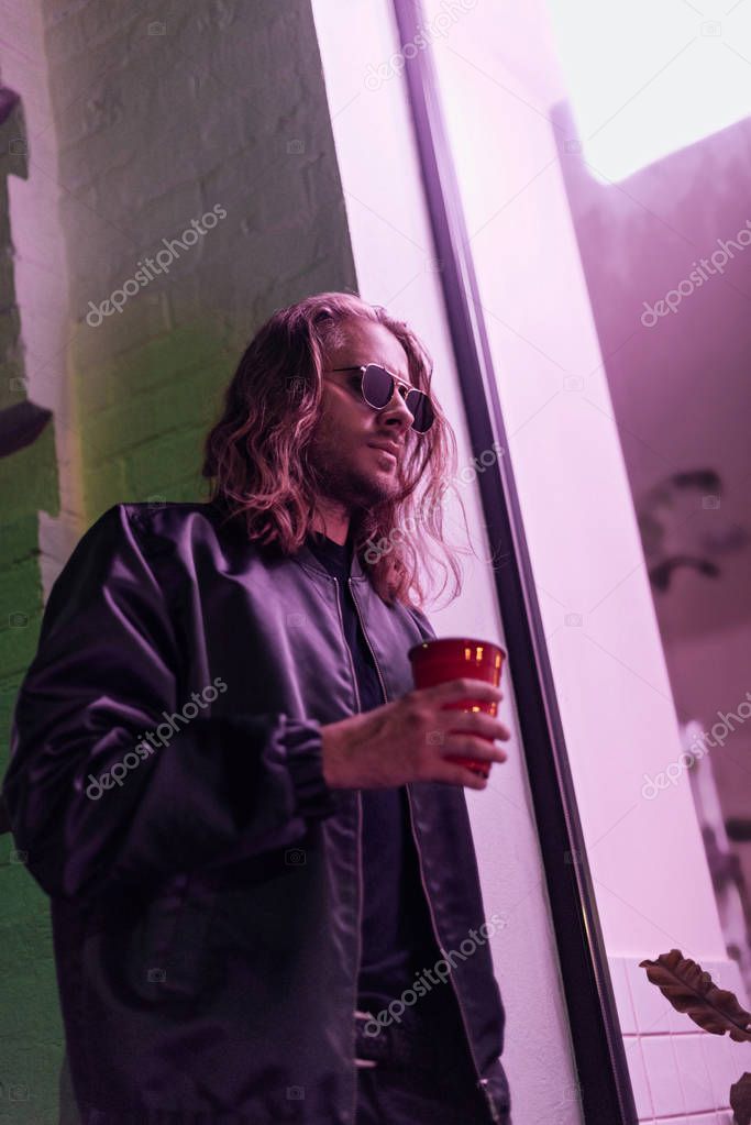 bottom view of young man with red plastic cup of drink on street at night under pink light