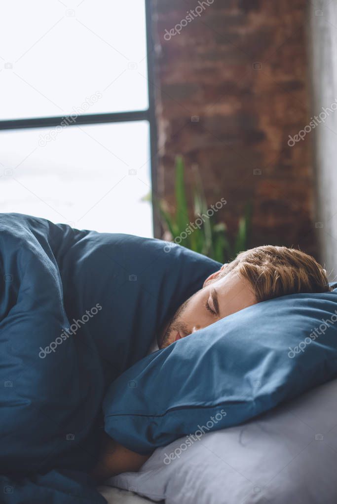 close up view of young handsome man sleeping under blanket in his bed at home