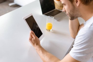 dizüstü bilgisayar ve bardak suyu mutfak masasında boş ekran ile dijital tablet kullanan adam 