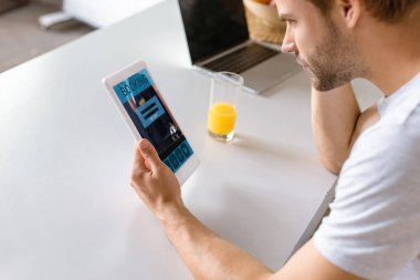Genç adam mutfak masasında Booking ekranda dijital tablet kullanma 