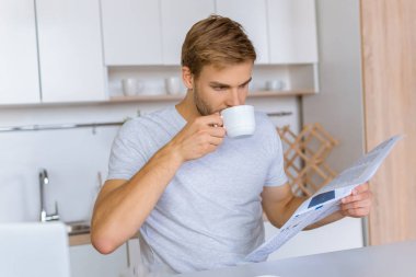 odaklı kahve içme ve mutfak masasında gazete okuyan genç adam 