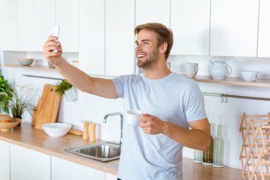 yakışıklı gülümseyen adam akıllı mutfak at selfie alarak kahve fincanı ile