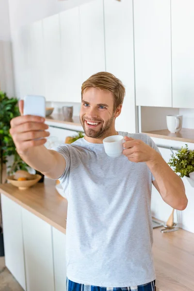 Sonriente Joven Con Taza Café Tomando Selfie Teléfono Inteligente Cocina — Foto de stock gratis