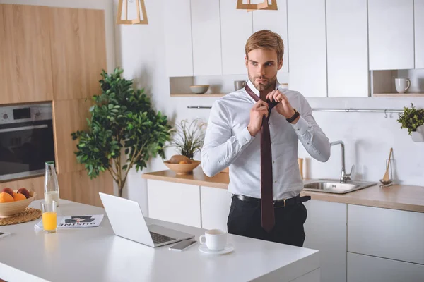 Geschäftsmann Weißem Hemd Bindet Krawatte Neben Küchentisch Mit Laptop Smartphone — Stockfoto