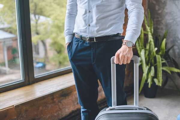 cropped image of businessman with hand in pocket standing with suitcase at home