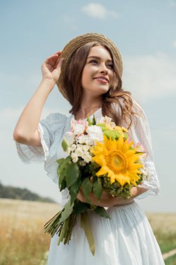 Beyaz elbiseli gülümseyen kadın portresi tarlada vahşi çiçekler Buket