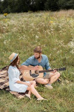 man playing acoustic guitar to girlfriend in summer filed clipart