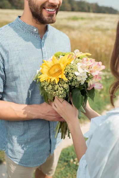 夏の畑でガール フレンドに野生の花の花束を提示する陽気な男のショットをトリミング  — 無料ストックフォト