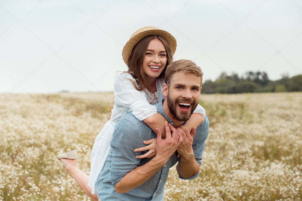 happy lovers piggybacking together in meadow with wild flowers