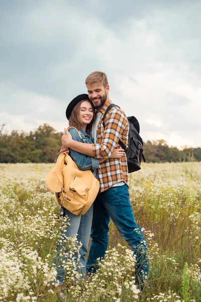 Pareja Joven Con Mochilas Abrazándose Campo Verano Con Flores Silvestres — Foto de Stock