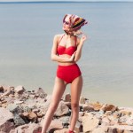 Menina bonita posando em biquíni vermelho e lenço elegante na praia rochosa