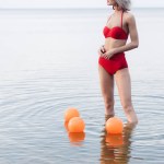 Przycięte widok kobiety w vintage czerwone bikini stojących w wodzie morskiej z pomarańczowe kulki