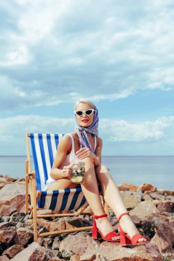 kavanoz kokteyl ile tutarak ve kayalık kıyısında plaj sandalye rahatlatıcı güneş gözlüğü güzel zarif kızı