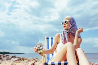 limonata tutarak ve kayalık sahilde şezlong içinde rahatlatıcı çekici moda kız