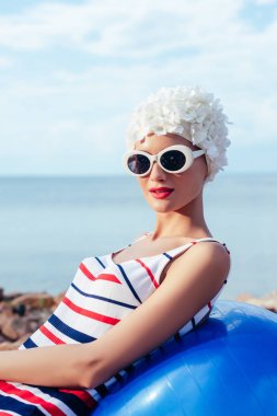 çizgili mayo, güneş gözlüğü ve beyaz şapka uygun topa rahatlatıcı genç kadın