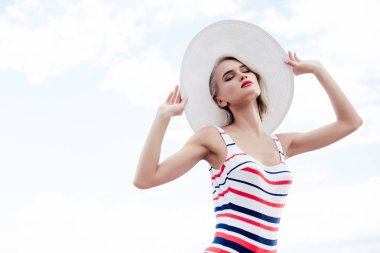 moda kız çizgili mayo ve yaz şapka, gökyüzü arka plan üzerinde poz
