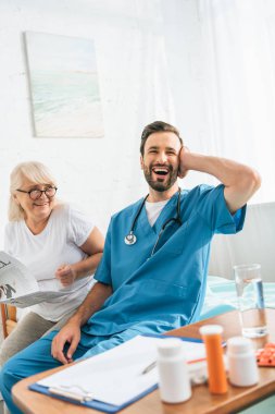 gazete tutan ve neşeli genç doktor hastane yatağı üzerinde otururken gülüyor bakarak gözlük mutlu üst düzey kadın