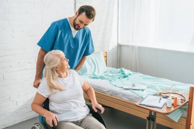 Erkek hemşire kadın kıdemli tekerlekli sandalyede bakarak gülen, yüksek açılı görünüş