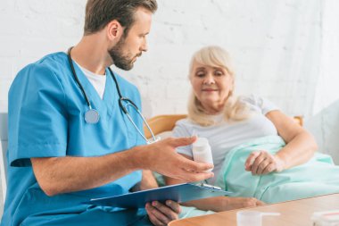 Pano tutarak ve yatakta yatan kadın kıdemli için hap gösteren doktor