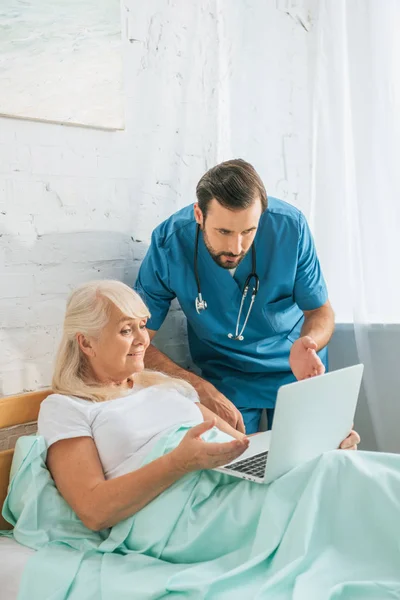 Joven Médico Con Estetoscopio Mirando Mujer Mayor Utilizando Ordenador Portátil — Foto de stock gratis