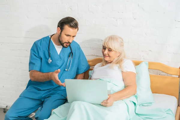 Verpleger Met Stethoscoop Zoek Naar Senior Vrouw Laptop Ziekenhuisbed Gebruikt — Stockfoto