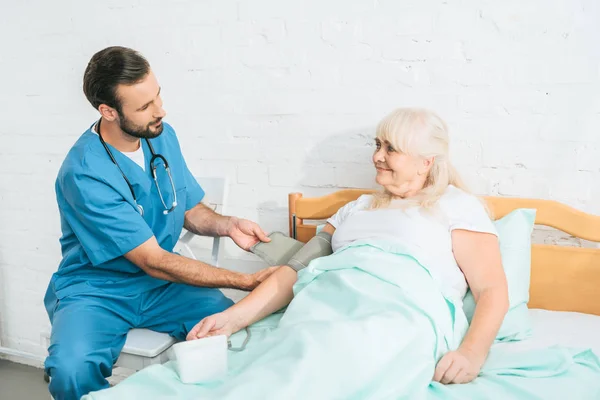 Junge Sozialarbeiterin Misst Blutdruck Bei Seniorin Die Bett Liegt — Stockfoto