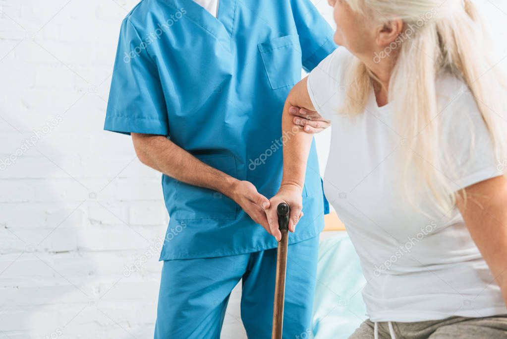 cropped shot of male nurse supporting senior woman with walking stick