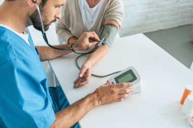 cropped shot of male nurse in stethoscope measuring blood pressure to senior woman clipart